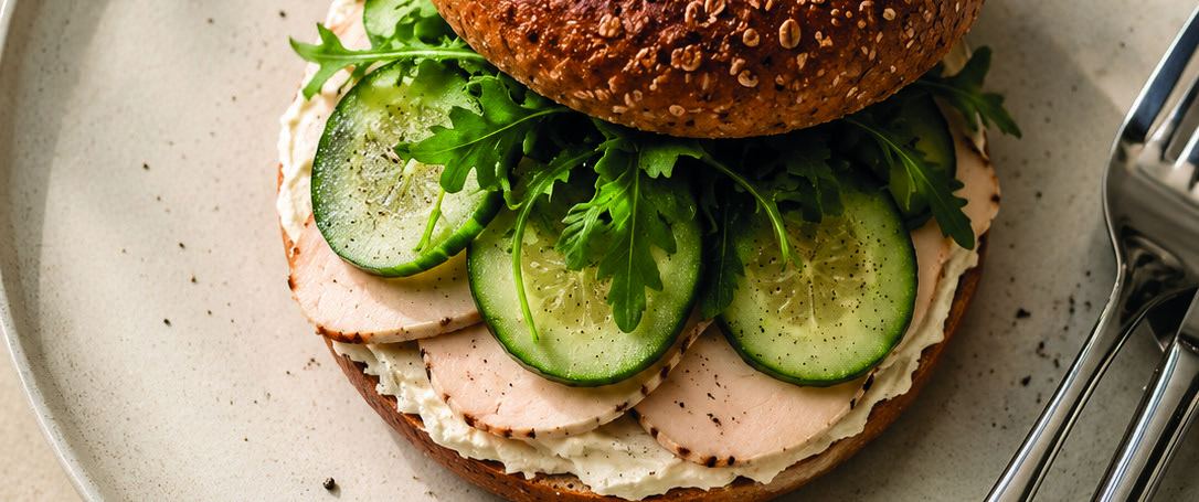 An open seeded bagel layered with cream cheese, turkey slices, cucumber and rocket.