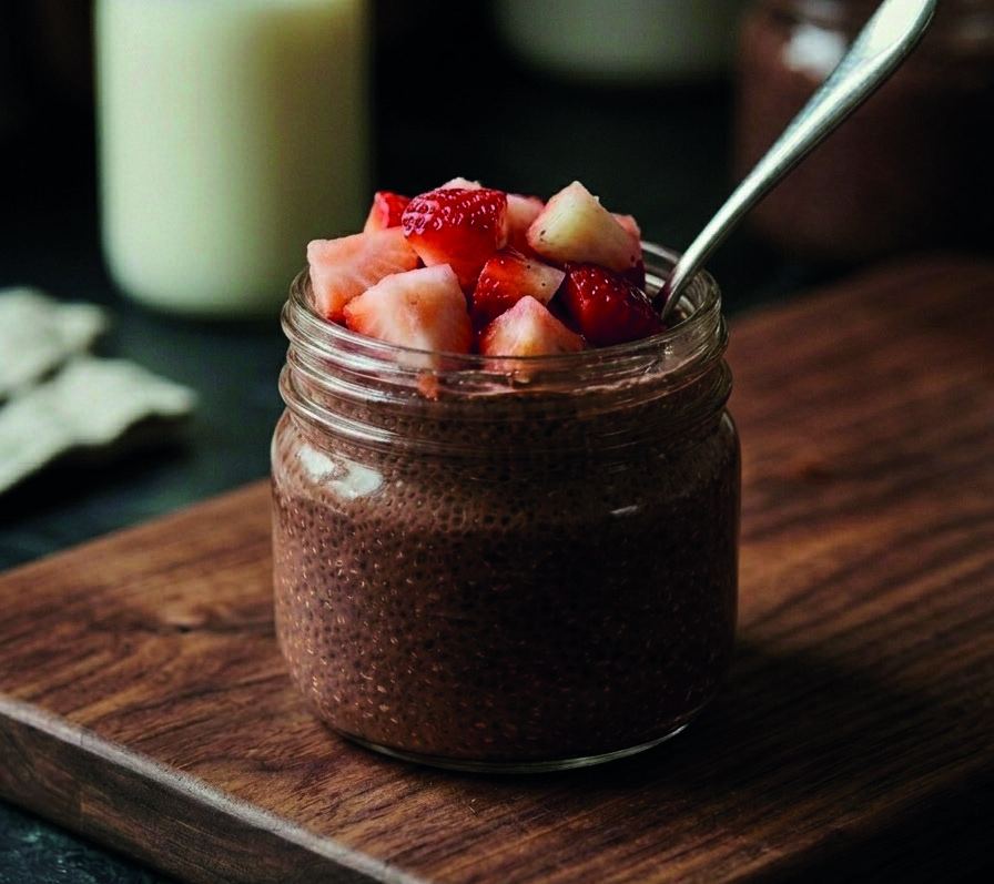 A jar of chocolate chia pudding topped with chopped strawberries, with a spoon resting in it.