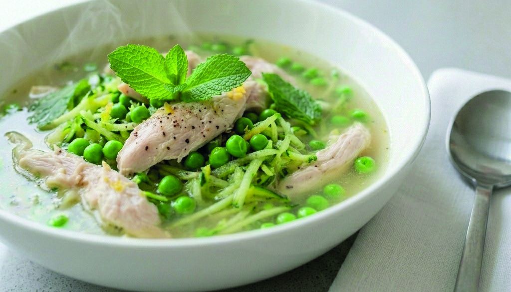 A bowl of poached chicken with peas, courgette and fresh mint in a light broth.
