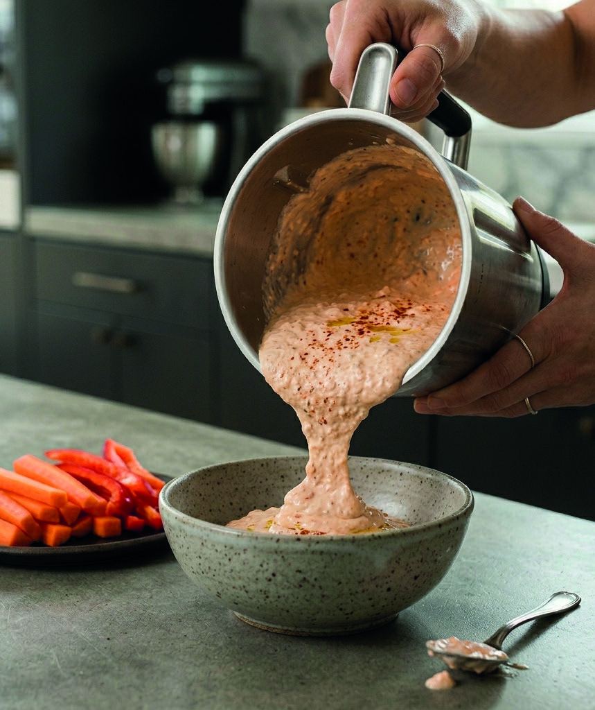 Whipped cottage cheese dip being poured into a bowl beside carrot sticks.