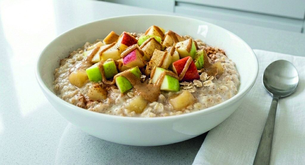 A bowl of porridge topped with diced apple, nut butter and cinnamon.