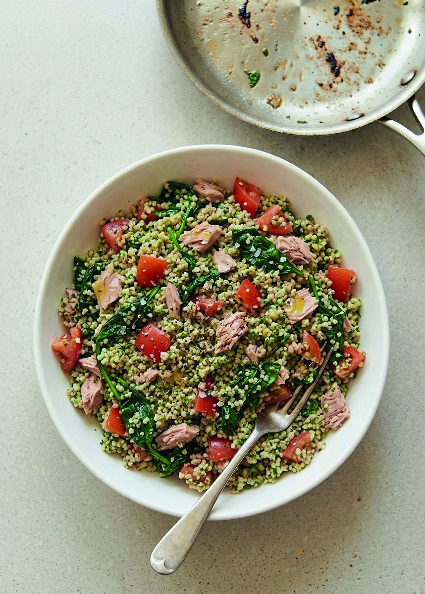 A bowl of quinoa salad with wilted spinach, tuna and diced tomato.